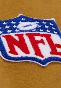 NFL logo patch in red, white, and blue yarn on a mustard yellow fabric background.