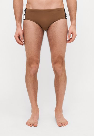 Bruine zwemboxers gemaakt van zachte stof, met een contrasterend logopatch op de heup en een klassieke low-rise pasvorm.