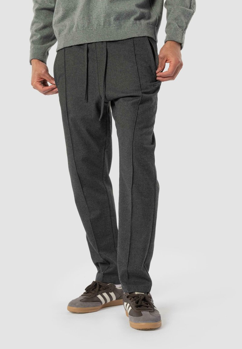 Jogging en gris foncé, taillé, fabriqué en tissu doux, avec une taille élastique à cordon, des poches latérales et de subtils détails de couture le long des jambes.