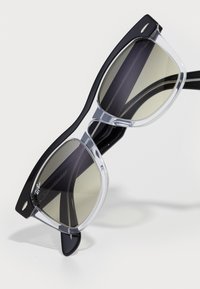 Musta ja kirkas muovinen kehys Ray-Ban aurinkolasit suorakulmaisilla tummennetuilla linsseillä valkoisella pinnalla.
