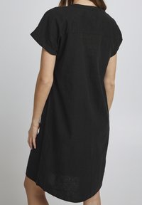 Abito corto in lino nero a maniche corte con vestibilità rilassata, scollatura rotonda e spacco laterale. Struttura sottile e lunghezza al ginocchio.