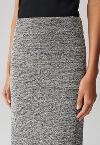 Jupe crayon tricotée en gris et noir avec un motif texturé, dotée d'une taille haute et d'un design ajusté, montrant des mains sur les hanches.
