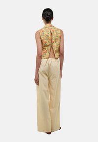 Haut sans manches à fleurs jaunes avec un dos découpé et un lien de fermeture, associé à un pantalon large à rayures jaunes et blanches.