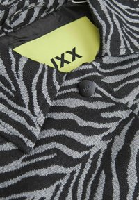 Juoda ir pilka zebra rašto striukė su tekstūriniu audiniu, turinti juodą sagą ir ryškiai geltoną vidinę etiketę su užrašu "JXX."