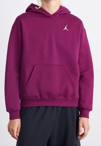 Sudadera morada hecha de una tela de textura suave. Presenta un bolsillo frontal y un logo Jumpman blanco en el pecho. Puños y dobladillo acanalados.