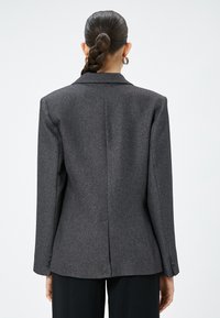Grijze op maat gemaakte blazer in textuurstof, met een gelapte kraag, enkele achterkantventilatie en met knopen sluitende manchetten, ontworpen met een ontspannen pasvorm.