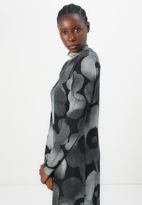 Long-sleeve dress in black with large gray floral patterns, featuring a high neckline and a smooth, soft texture.