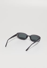 Juodos ovalios saulės akinių rėmeliai su tamsiais stiklais, atidaryti gulintys ant baltos paviršiaus, matoma Ray-Ban logotipas ant vieno iš šonų.