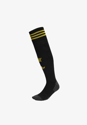 Black knee-high socks with yellow stripes at the top, featuring textured material and a gray toe and heel. Logo printed on the front.