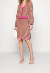 Ensemble de cardigan tricoté et de jupe en rose et beige avec des motifs géométriques, comprenant une fermeture à boutons, des manches longues et des accents côtelés.