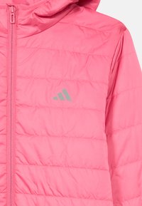 Veste matelassée rose avec capuche, présentant des coutures horizontales et un logo argenté sur la poitrine. Texture lisse et fermeture éclair à l'avant.