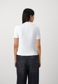 Witte geribde gebreide top met korte mouwen, voorzien van een ronde halslijn en een aansluitend ontwerp, gecombineerd met hoge taille donkerblauwe jeans.