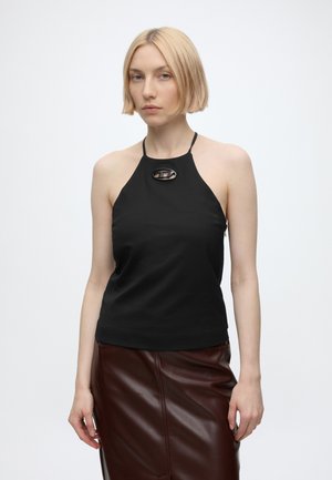 Femme aux cheveux blonds courts portant un haut dos-nu noir avec une boucle décorative et une jupe en cuir brun foncé sur fond blanc.