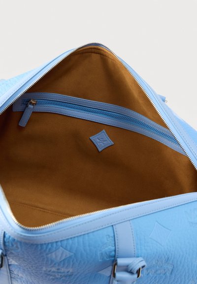Ανοιχτή τσάντα από ανοιχτό μπλε δέρμα που αποκαλύπτει ευρύχωρο ταμπά εσωτερικό με μπλε τσέπη με φερμουάρ και ανάγλυφο λογότυπο.