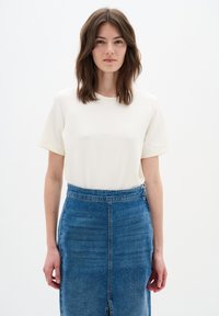 Top crem cu mânecă scurtă, asortat cu o fustă din denim cu croi drept, având o fanta frontală și un finisaj texturat de culoare albastră.