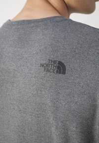 Šedé bavlněné tričko s kulatým výstřihem a krátkými rukávy, na horní části zad je černé logo "The North Face".