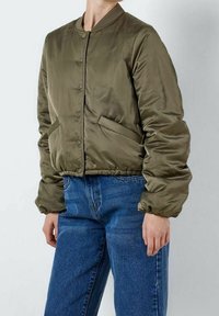 Olivgrön bomberjacka i glatt, glansigt material, med knappstängning fram, ribbad krage och sidofickor. Stylen med lösa jeans.