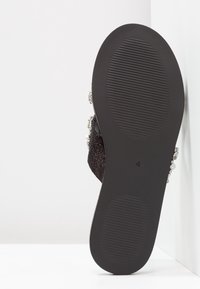 Svart slip-on-sandal med texturerad yta, dekorerad med silverdetaljer och en räfflad gummisula för grepp. Märkt storlek 4.