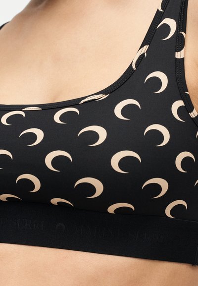 Εγγύς πλάνο ενός μαύρου αθλητικού σουτιέν με μπεζ μοτίβο ημισέληνου και φαρδιά ελαστική ταινία κάτω από το στήθος.
