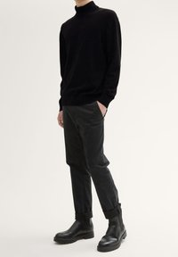 Svart polotröja, svarta smala byxor och svarta ankelstövlar. Mjuk textur, åtsittande design, med ett avslappnat utseende.