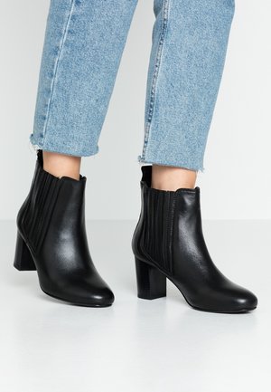 Ben iført lyseblå cropped jeans kombineret med sorte læderankelstøvler med blokhæle og elastiske sider.