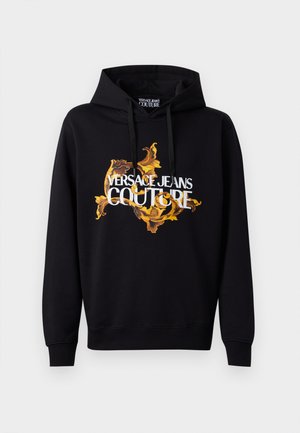 Black hoodie featuring a vibrant gold and yellow baroque pattern and white "VERSACE JEANS COUTURE" text on the front. Drawstring hood.