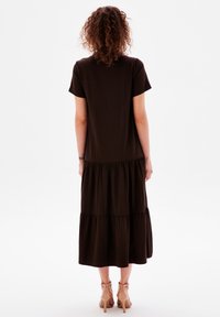 Braunes, geschichtetes Maxikleid mit kurzen Ärmeln, das über eine weiche Textur und ein fließendes Design verfügt. Getragen mit hellen Absätzen.