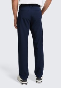 Pantalones azul marino de tejido suave, con corte recto, bolsillos traseros y combinados con zapatillas blancas y negras.