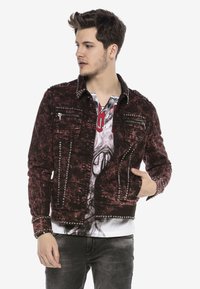 Rote und schwarze Jeansjacke mit metallischen Nieten entlang der Nähte, an den vorderen Taschen und am Kragen. Abgenutzte Textur, Knopfverschlüsse und eine taillierte Passform.