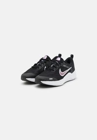 Chaussures de sport noires avec une pointe arrondie, tige en mesh, semelle blanche contrastante et accents violets sur la languette et le logo.