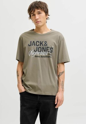 Olijfgroene katoenen t-shirt met korte mouwen, met een grafische print van "JACK & JONES Superior" in zwart en wit. Zwarte denim jeans.
