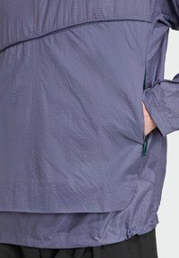 Purple, textured jacket with a half-zip design, side pockets, and adjustable hem. Features a subtle grid pattern and elastic cuffs.