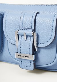Light blue textured leather handbag with a flap closure, silver hardware, and 'Michael Kors' branding on the buckle.