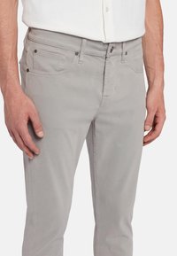 Chinos gris clair en mélange de coton doux. Présentent des poches latérales, une fermeture à bouton et des coutures contrastées pour un détail supplémentaire.