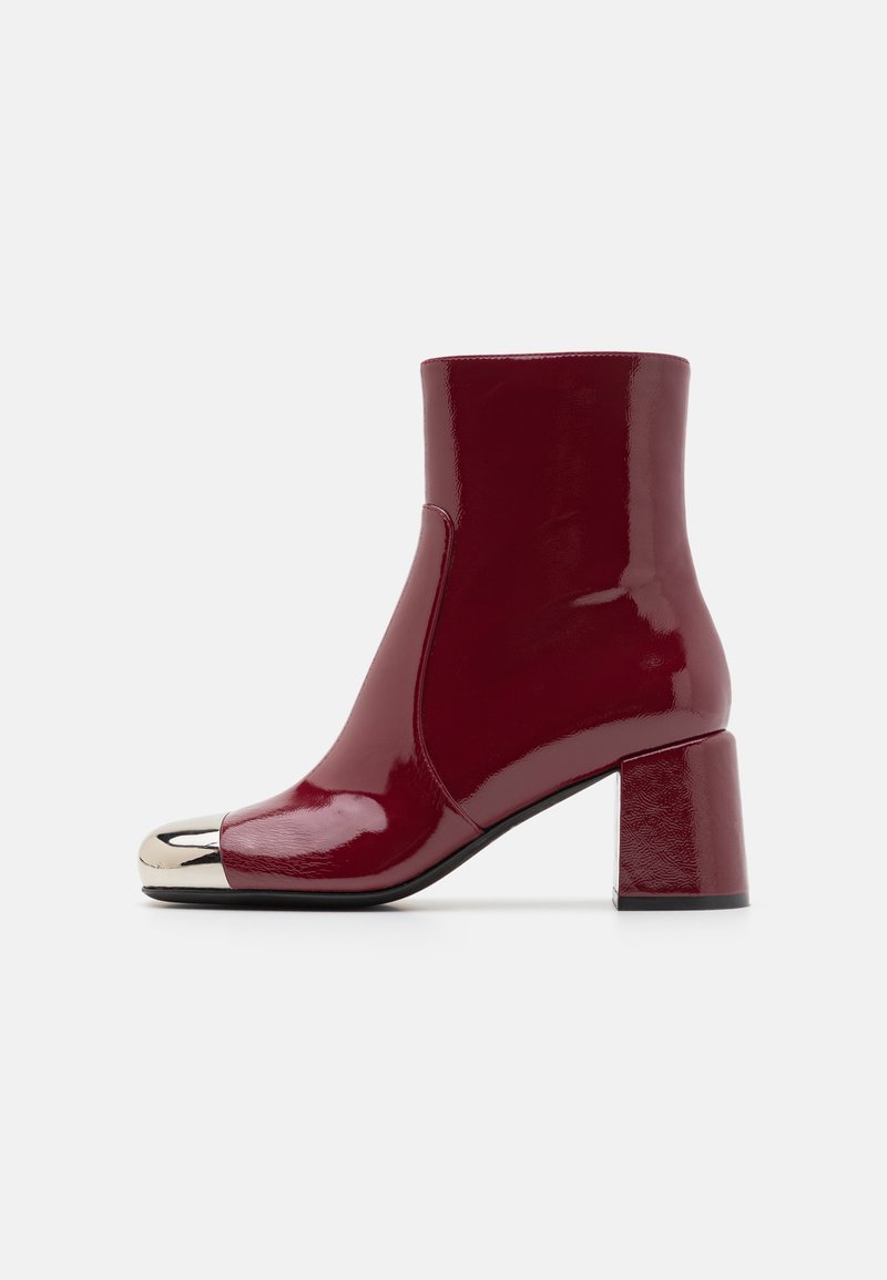 Burgundy patent leather ankle boot with a rounded toe, metallic cap, and a square block heel. Smooth texture and sleek design.