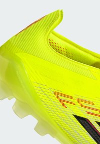 Ποδοσφαιρικό παπούτσι σε λάιμ πράσινο με υφή πλέγματος στο πάνω μέρος, αντανακλαστικές ασημένιες ρίγες και κόκκινες λεπτομέρειες. Διαθέτει χαμηλό κόψιμο και διαφανές πέλμα.