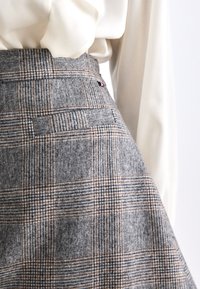 Grijze geruite rok gemaakt van textuurstof. Kenmerkt zich door een hoge taille, zijzak en subtiele bruine en zwarte ruitpatronen.