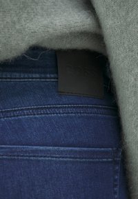 Jeans de color azul marino con una etiqueta de cuero negra que dice "BOSS", combinados con un suéter de lana gris que muestra una textura suave.