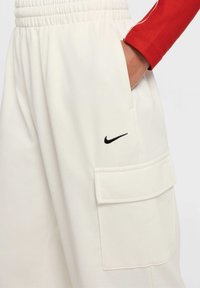 Białe dresy z żebrowanym paskiem w talii, z boczną kieszenią i małym czarnym logo Nike z przodu. Miękka, teksturowana tkanina.