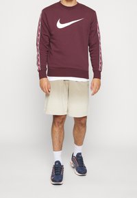 Maroon Nike sweatshirt with white logo, paired with beige shorts and dark athletic shoes. Features striped accents on sleeves.