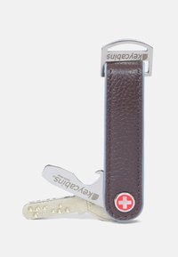 Brown leather key holder with a silver metal clip, featuring Swiss emblem. Includes a metallic key with textured surface.