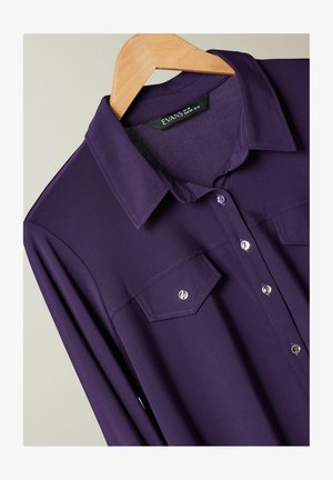 Lila Langarmhemd mit klassischem Kragen, zwei Brusttaschen und silbernen Knöpfen. Hergestellt aus glattem, strukturiertem Stoff.
