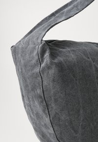 Grå stoffveske med en myk, teksturert overflate. Har en bred stropp og glidelås. Enkel, rund form med synlige sømmer.