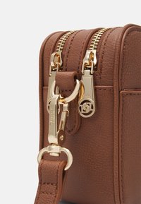 Brązowa torebka ze skórki o teksturze z złotymi zamkami, okuciem i zapięciem. Kompaktowy design z odpinanym paskiem i detalem logo.