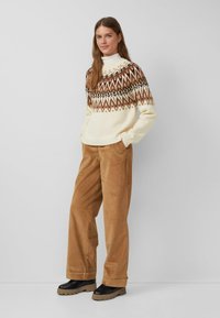 Gebreide trui in crème met bruine geometrische patronen, gecombineerd met lichtbruine corduroy broeken en zwarte stevige laarzen met een dikke zool.