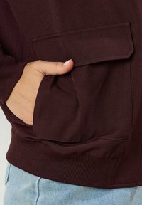 Bordeaux sweatshirt met een voorzak, gemaakt van een textuurstof, met ribgebreide uiteinden en een ontspannen pasvorm, gecombineerd met lichtblauwe jeans.