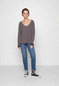 Top de manga comprida às riscas em cinza escuro com riscas brancas, design com decote em V, combinado com jeans azuis e ténis pretos de cano alto. Fundo liso.