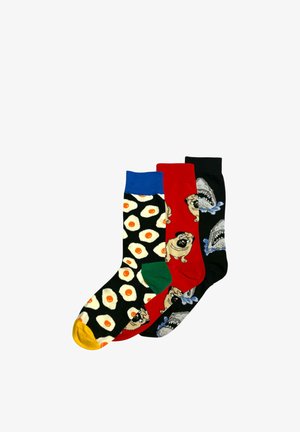 Trzy kolorowe skarpetki: jedna z jajkami sadzonymi na czarnym tle i żółtym palcem u nogi, druga czerwona z mopslami i zielonym piętą, trzecia czarna z rekinami i rozbryzgami wody.