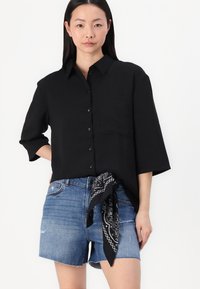Black button-up shirt with a pocket, paired with frayed denim shorts. A black and white bandana is tied at the waistband.