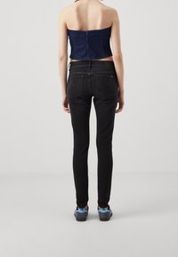 Top sin tirantes de mezclilla con cremallera y jeans ajustados negros. La modelo lleva zapatillas azules y grises con un diseño texturizado y detalle de cordones.